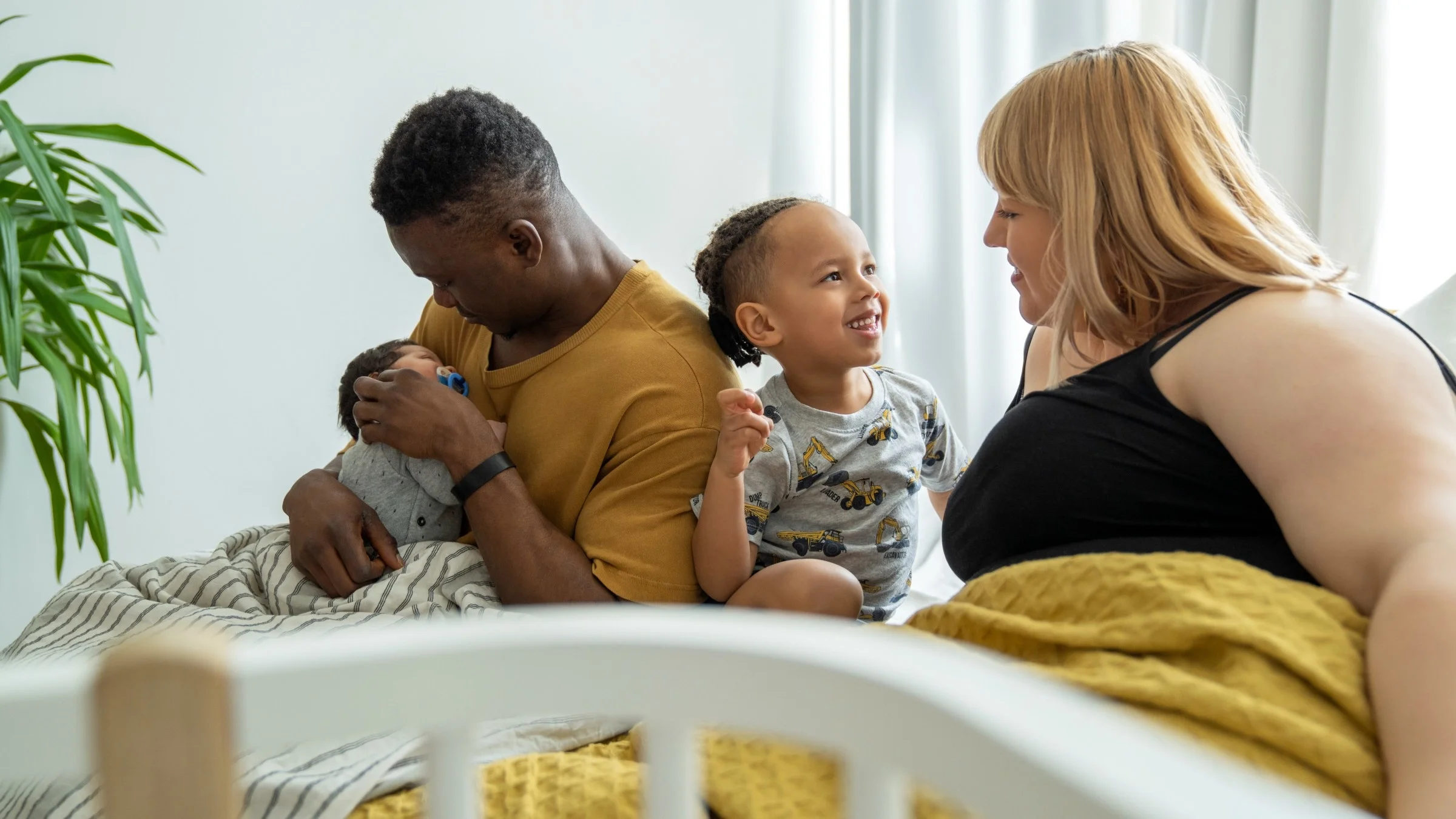 Una familia sentada en su cama con un niño pequeño y un bebé.