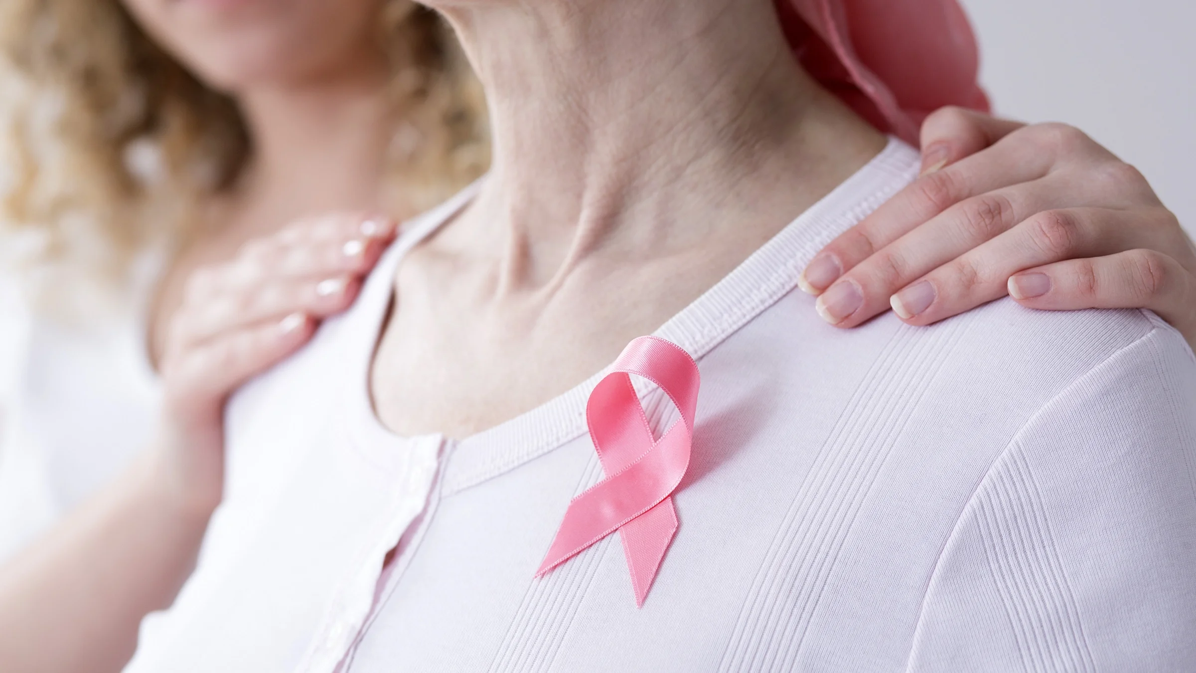 Woman with cancer wearing a pink ribbon, supported by her daughter