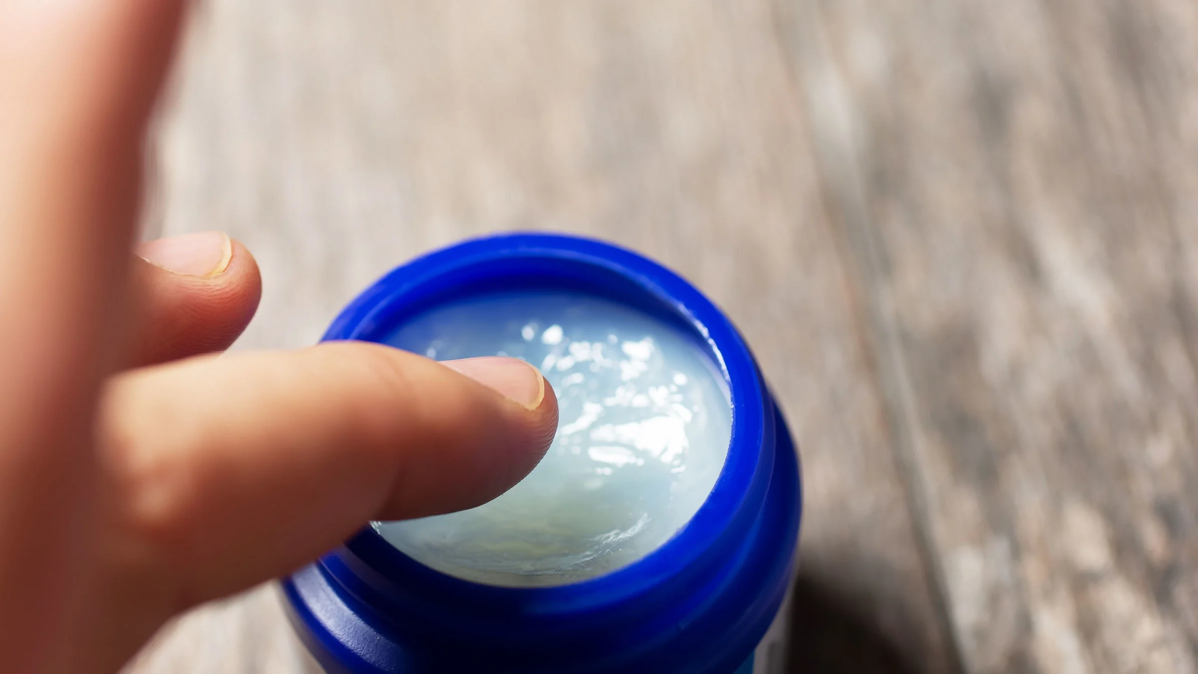 A close-up image shows a finger dipping into a jar of VapoRub.