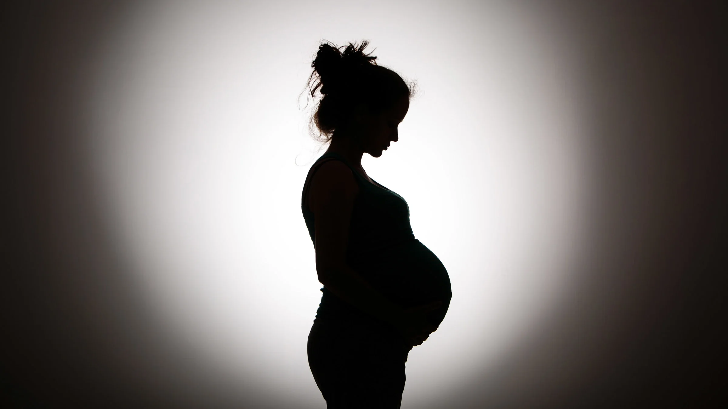 The side silhouette a pregnant person.