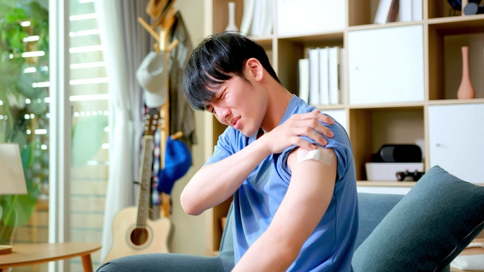 A person with a vaccine bandaid on their arm experiencing body aches.