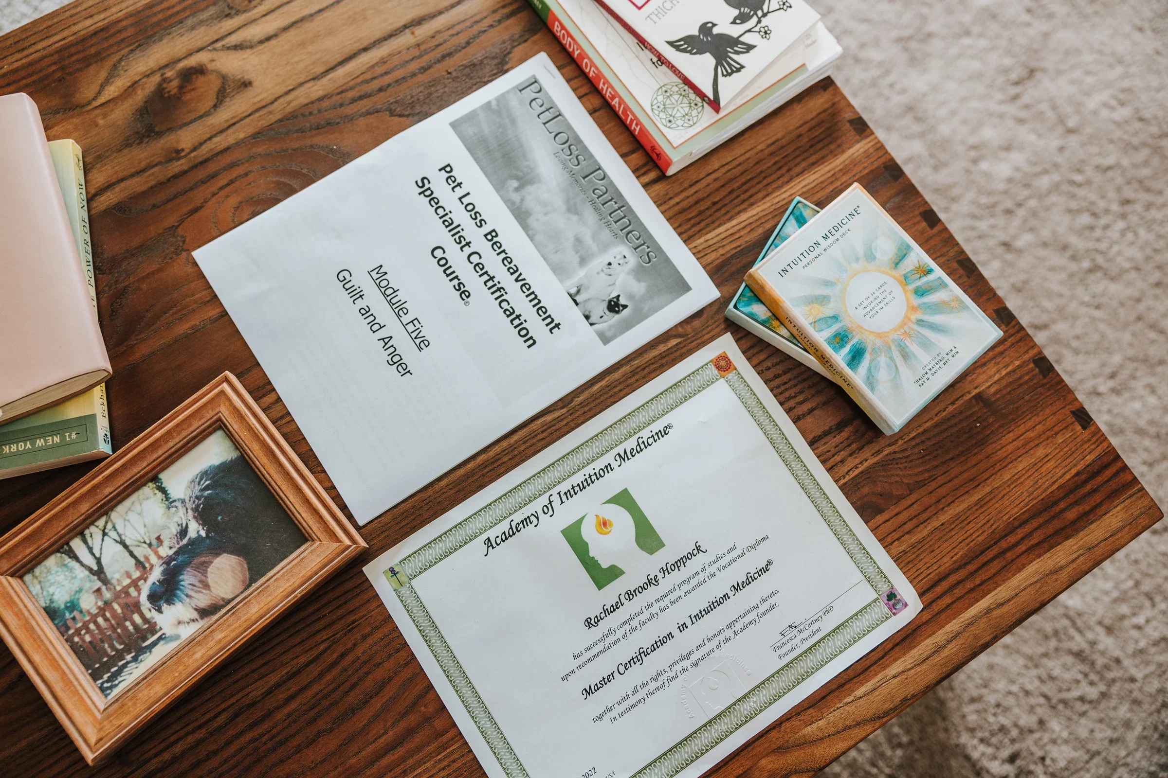 A photo shows Rachael Brooke Hoppock’s certification from PetLoss Partners and reference materials on a wooden table.
