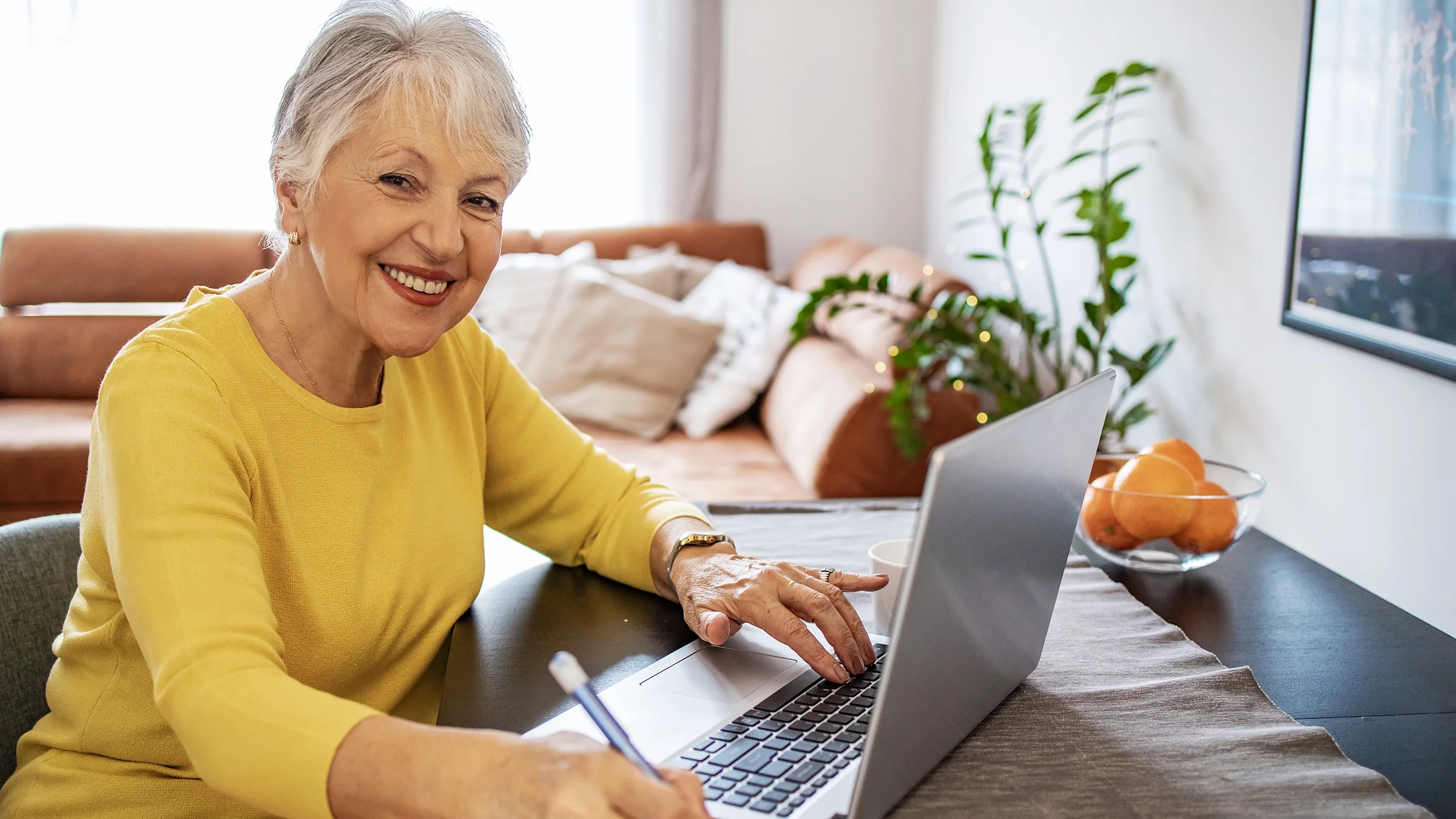 An older woman is smiling while using a laptop.