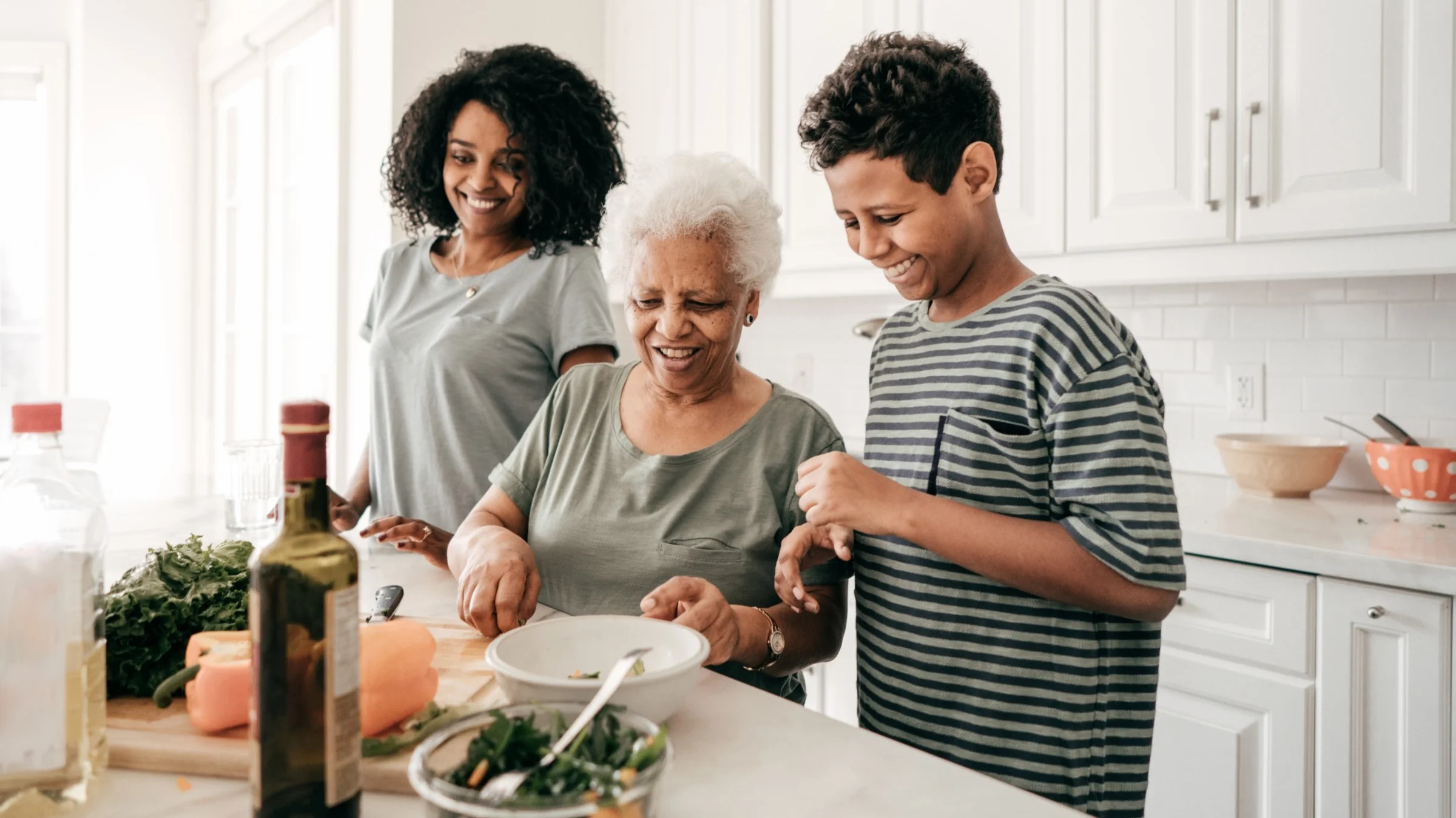 Elderly grandmother teaching her two grandkids how to cook in a bright white kitchen.