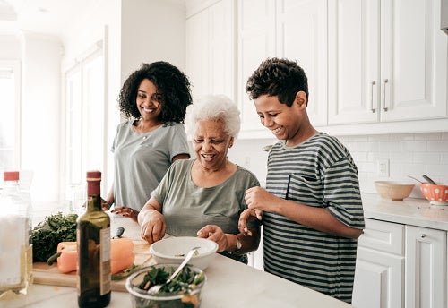 Elderly grandmother teaching her two grandkids how to cook in a bright white kitchen.