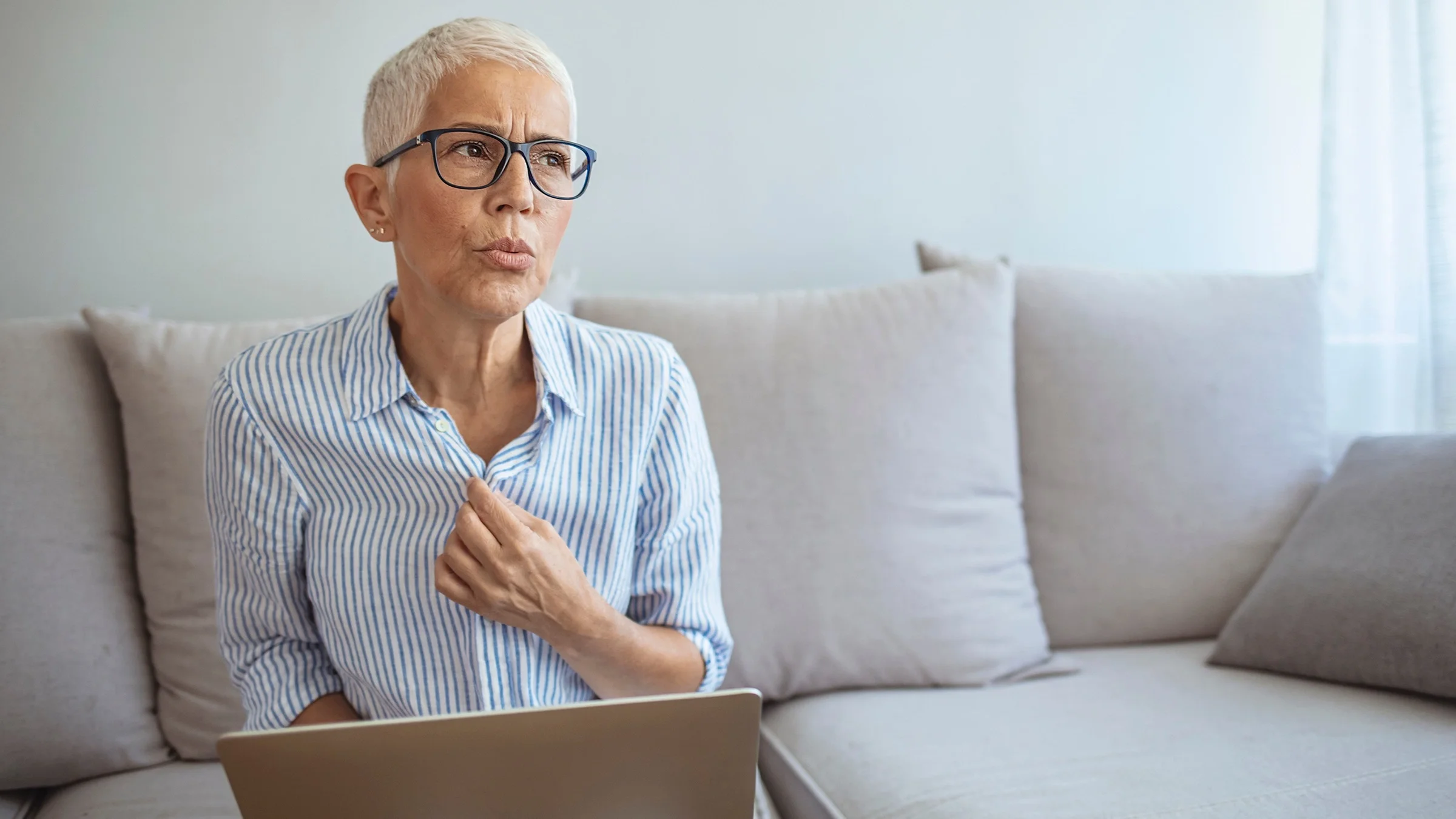 Portrait of a middle aged woman having a hot flash. She is sitting on her couch with a laptop in her lap.