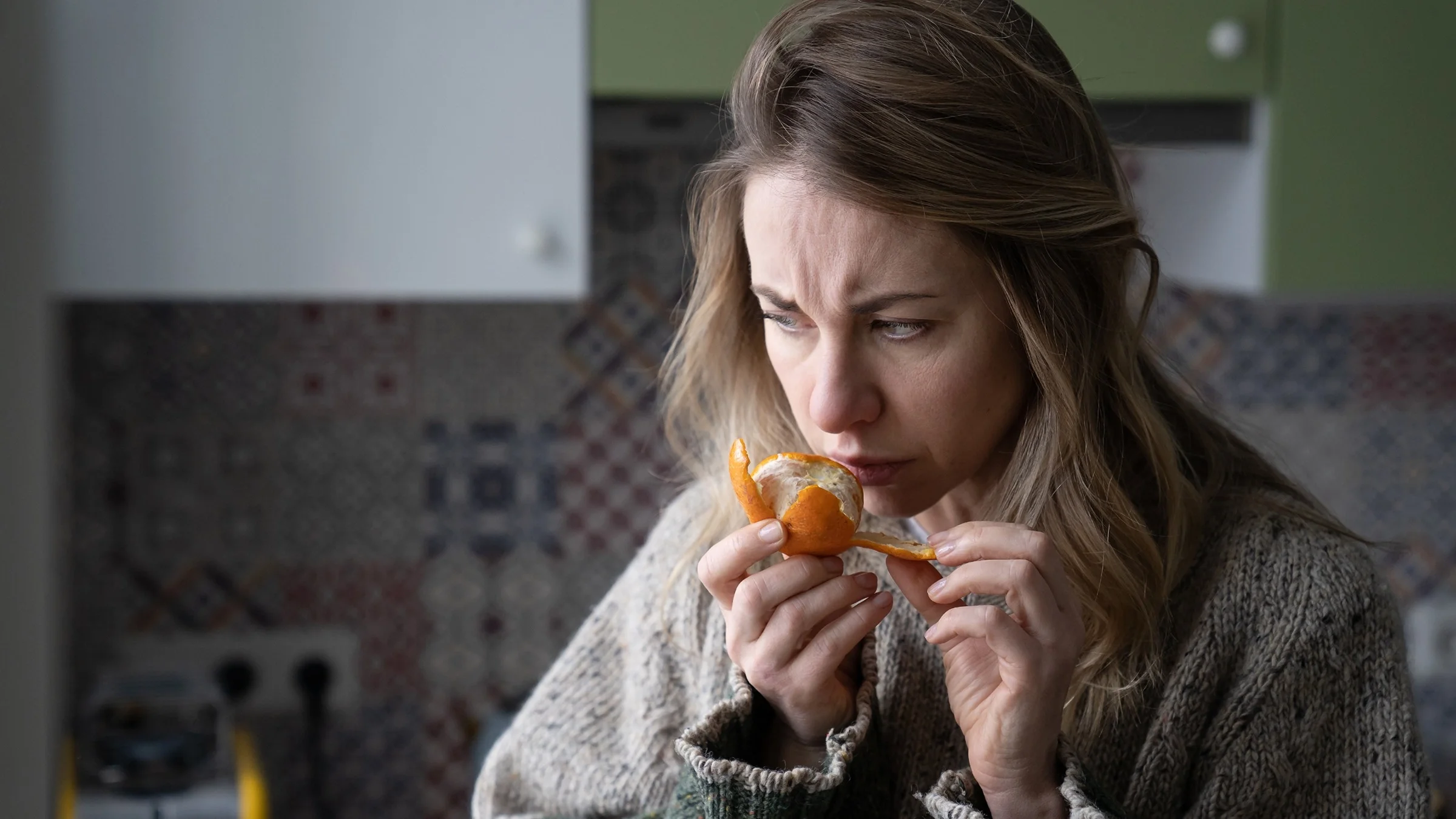 Portrait of a woman smelling a small orange. She has a concerned look on her face.