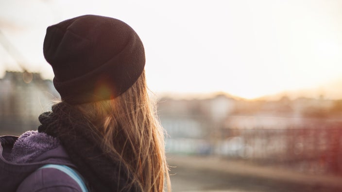 Portrait of a young woman in a beanie looking off at the sunset.