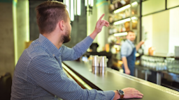 A person raising their hand to order a drink at a bar.
Artem Peretiatko/iStock via Getty Images Plus 