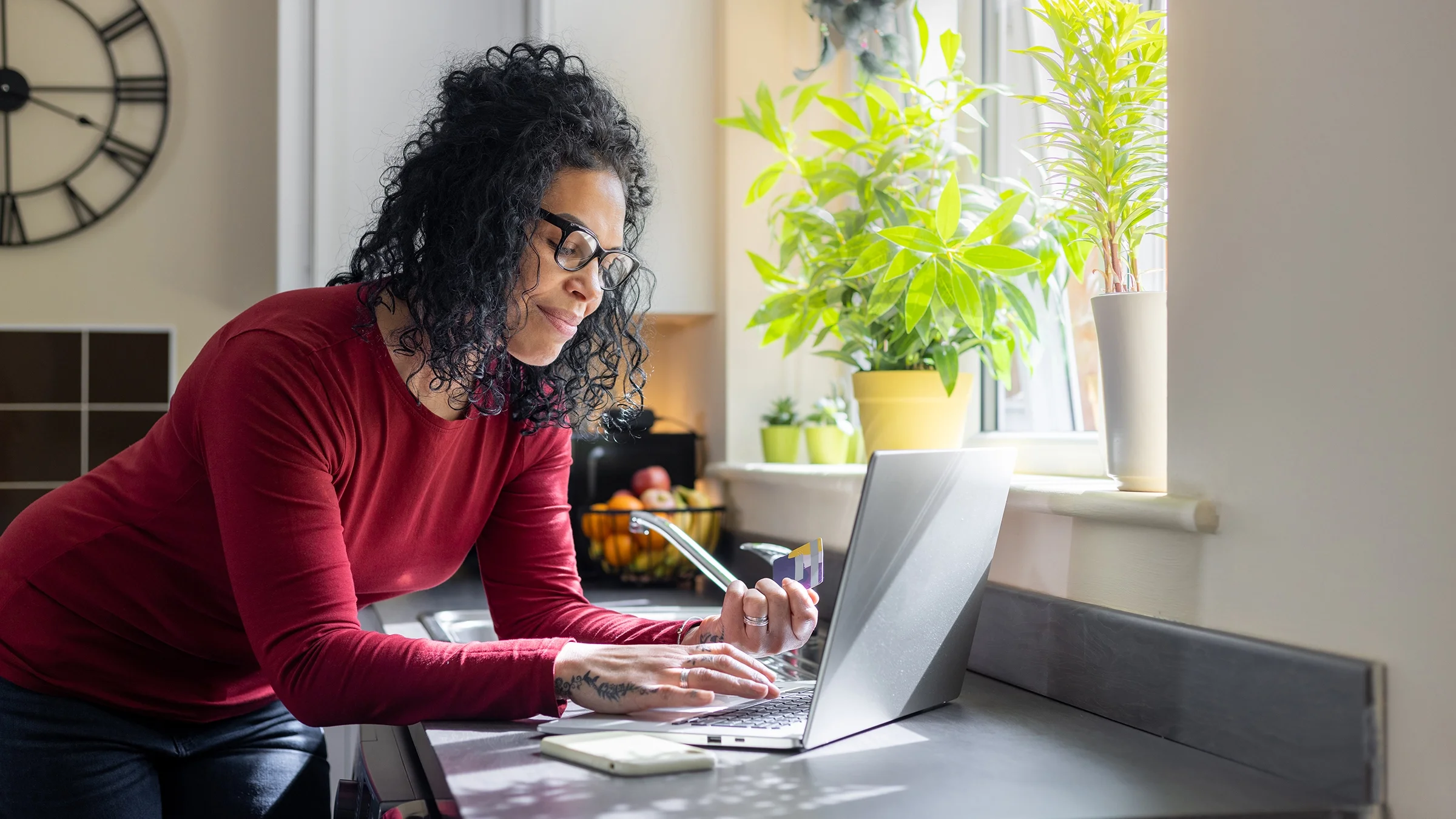 A woman stands in her kitchen and pays a bill online.