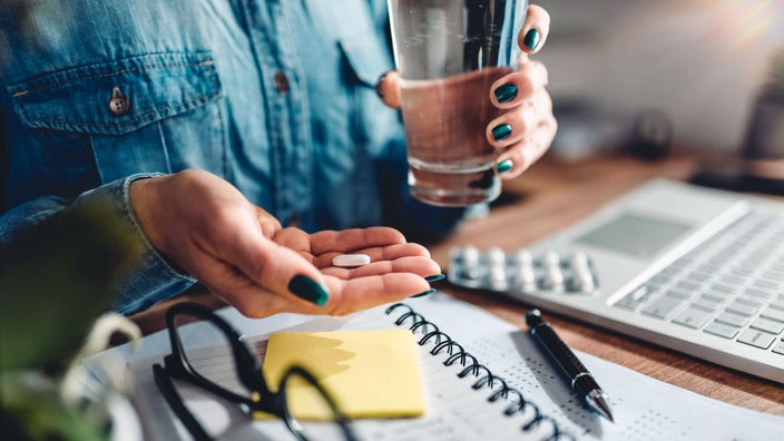 Close-up woman taking daily medication sitting at desk.