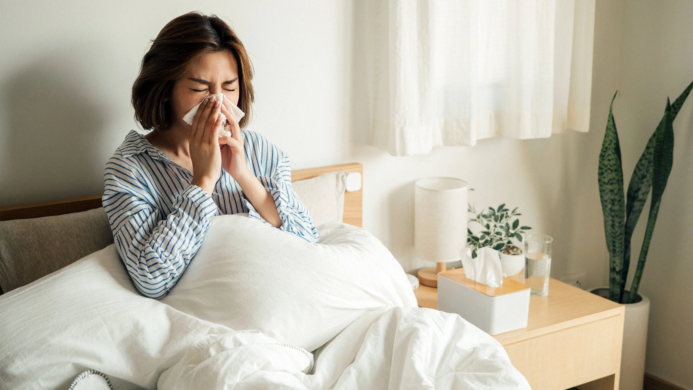 A woman blows her nose into a tissue while in bed. Colds and sinus infections share some symptoms, but there are ways to tell them apart.