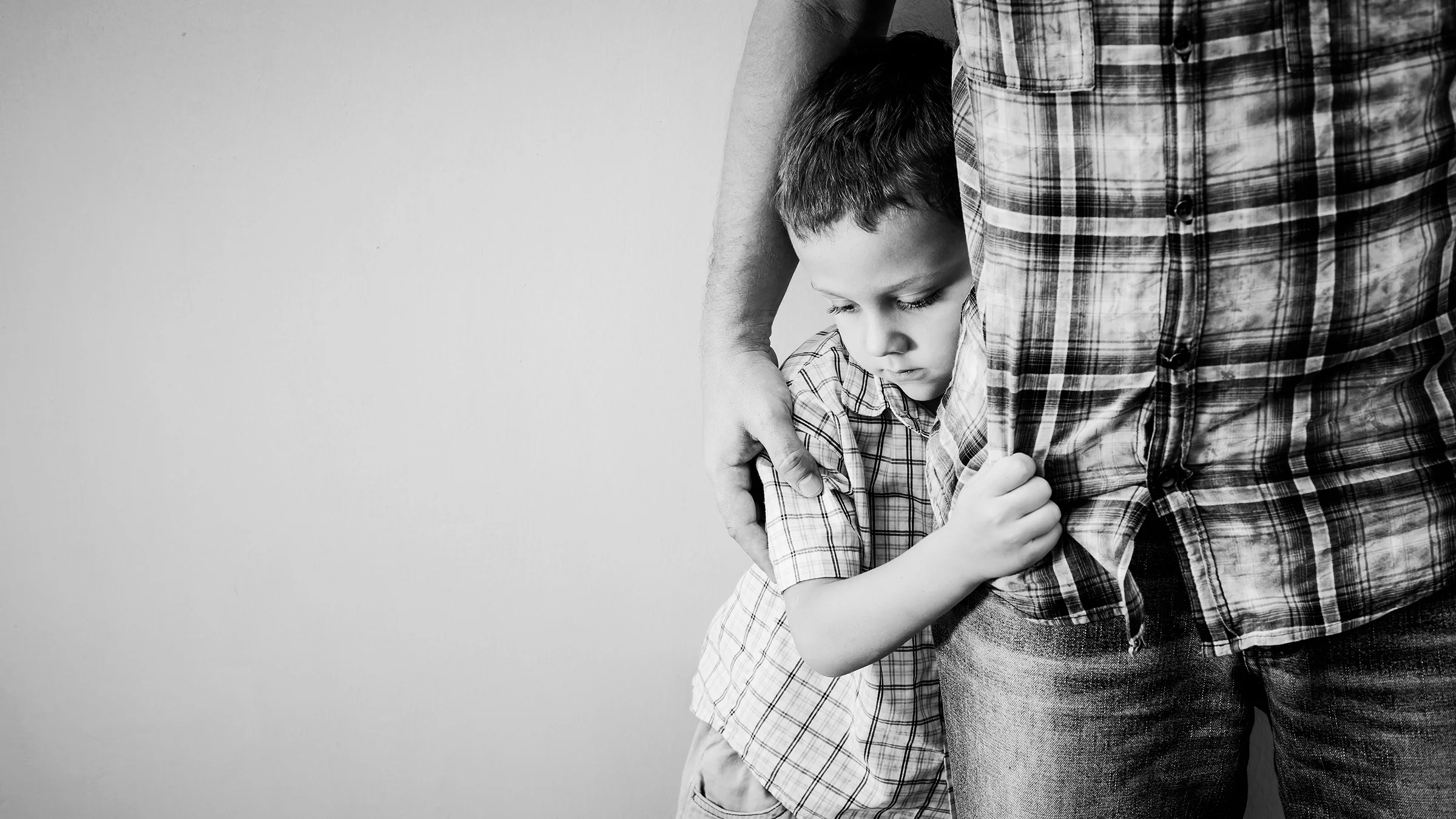 Black and white photo of a young boy hugging his dad's leg.