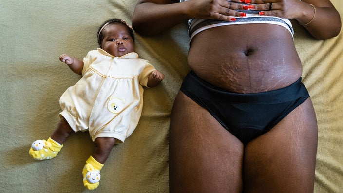 Cropped shot of a woman on a bed next to her newborn. The focus is on her belly with stretch marks and the baby.