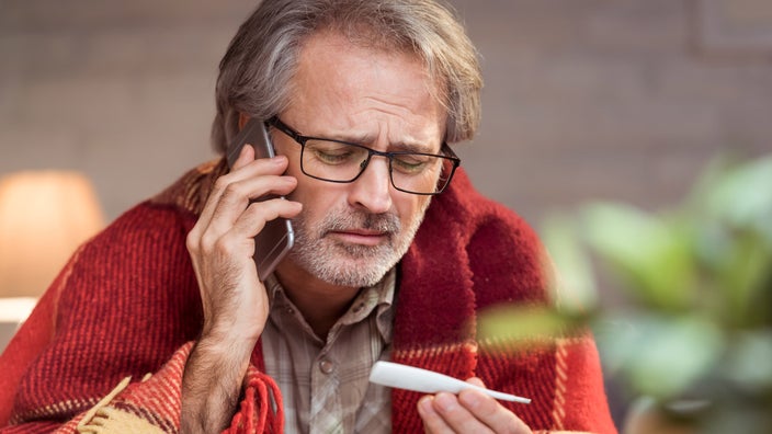 Woman sitting up in bed taking her temperature with a thermometer. 