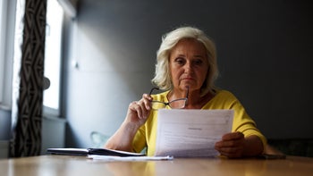 Research: Healthcare Access: Insurance: senior woman reading paperwork 1349148610