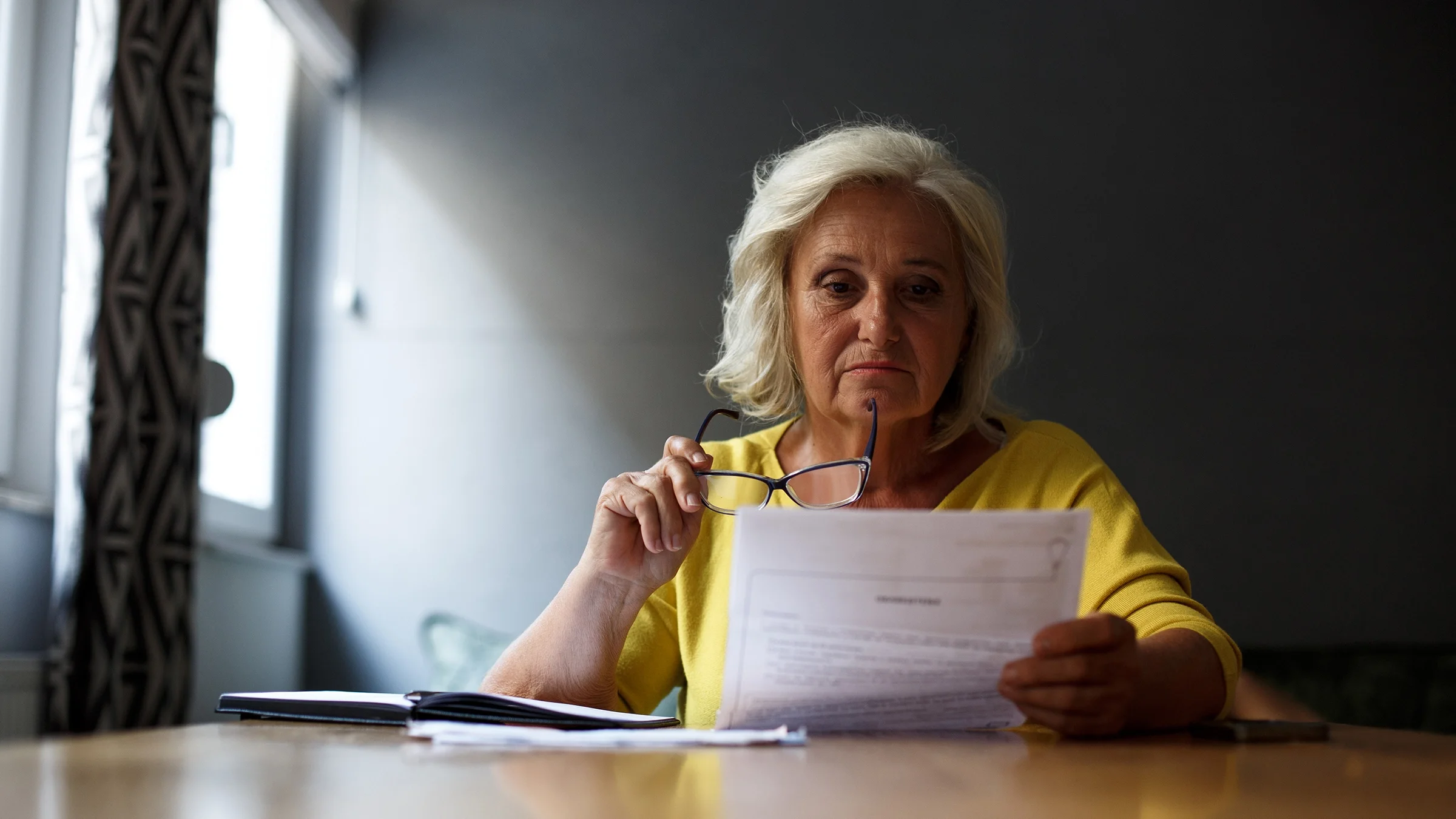 A woman sits at a table reading paperwork.