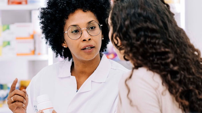 Young Black pharmacist talking to customer while holding a white medicine bottle.