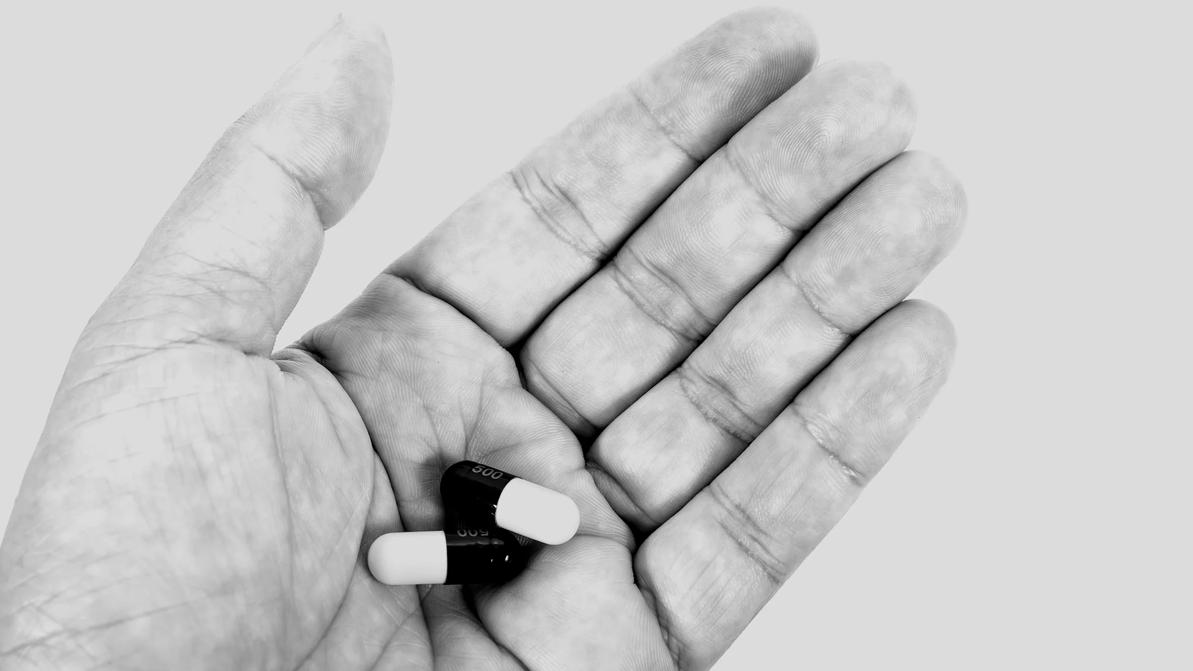 Black and white image of a person's hand holding two black and white pills in their palm.