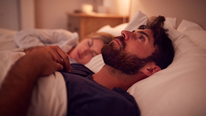 A man is lying wide awake in bed next to his partner.