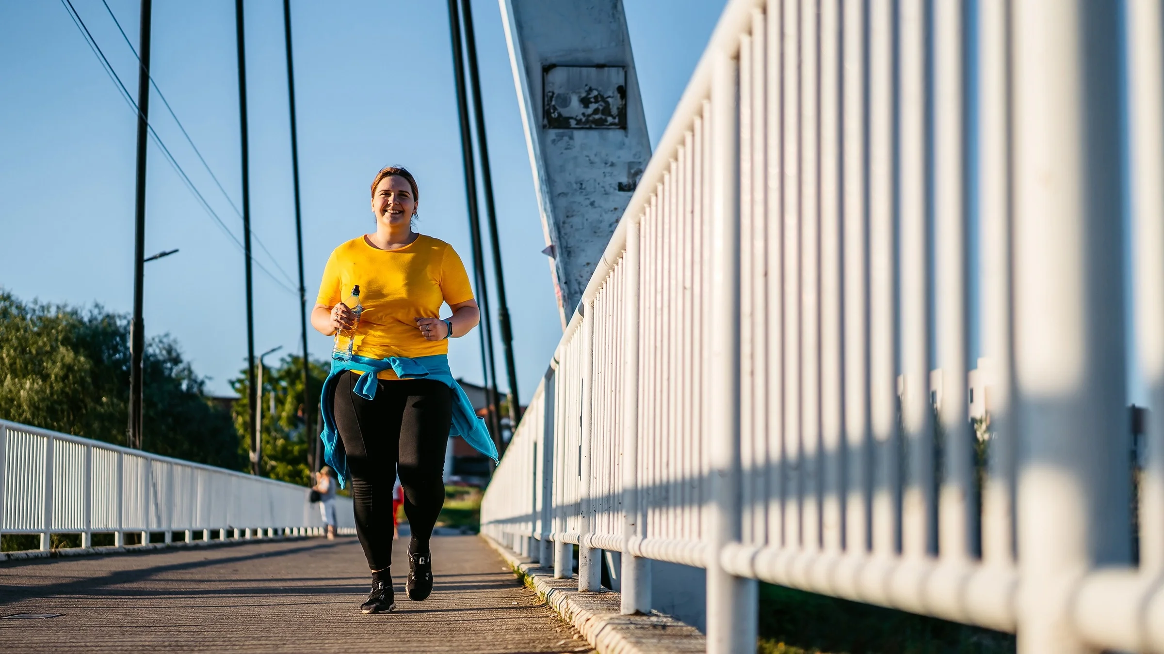Larger woman on a run on a bright blue sunny day. She is running across a bridge.