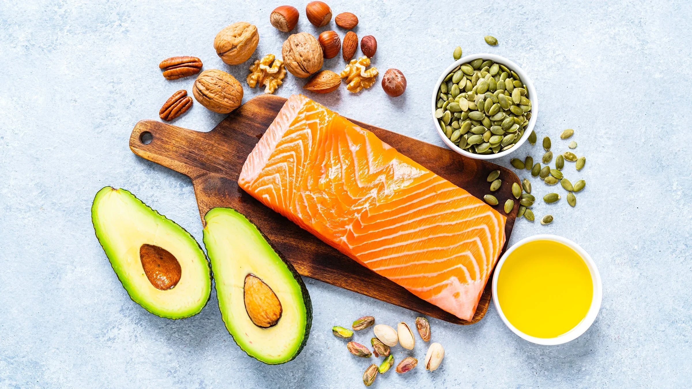 Foods high in healthy fats like salmon, avocado, and nuts are displayed on a table. 