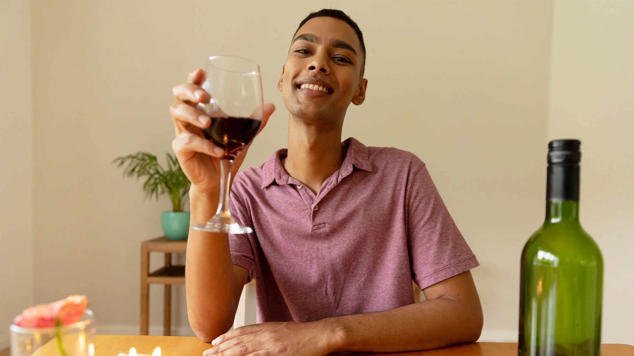 A man holds a glass of red wine and smiles at the camera.