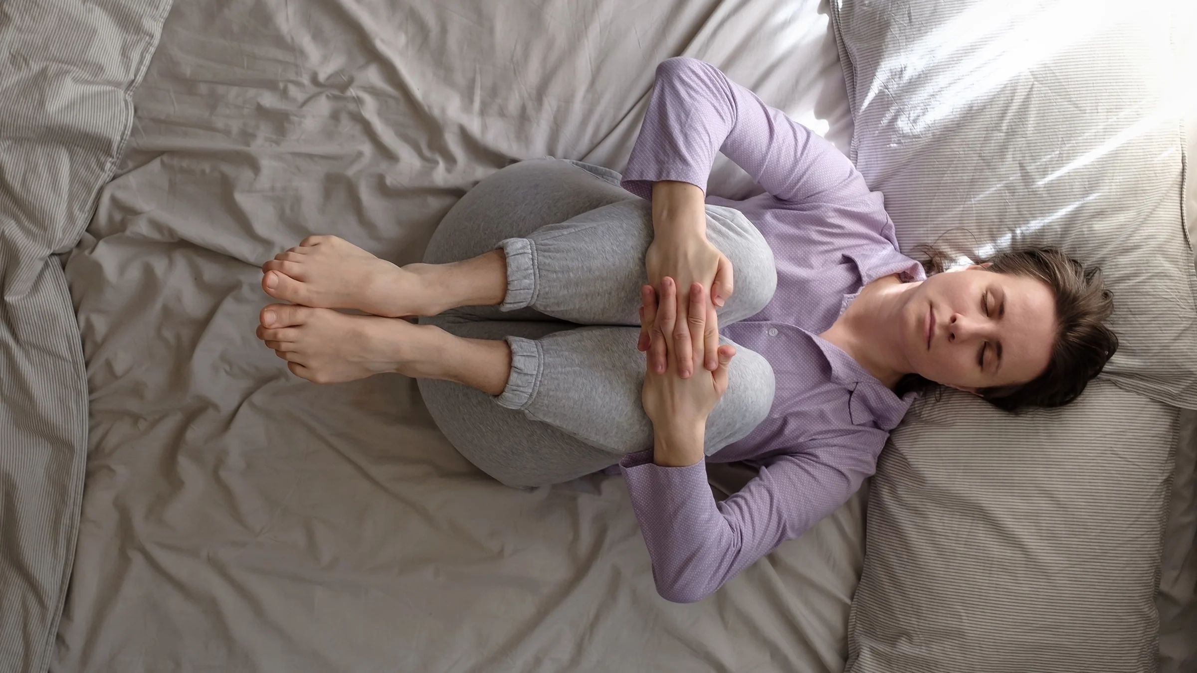 A woman does a knee-to-chest pose in bed. 
