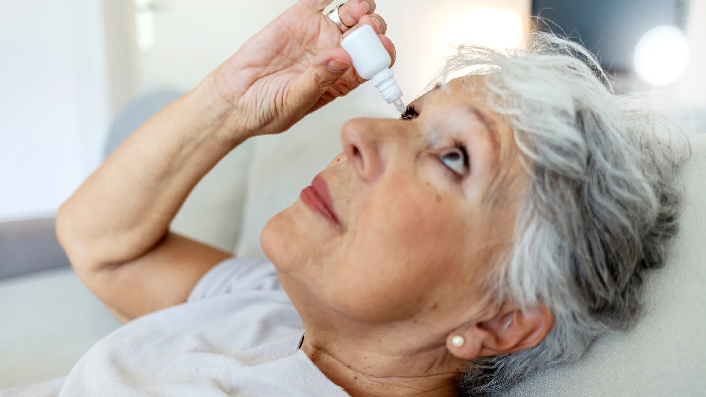 A woman leans back as she uses eye drops.