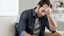 A man sits at home holding his head and looking distraught.
Goodboy Picture Company/E+ via Getty Images