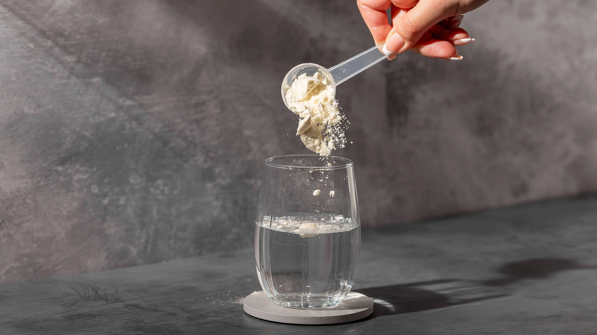 Close-up hand mixing supplement powder in a glass of water.