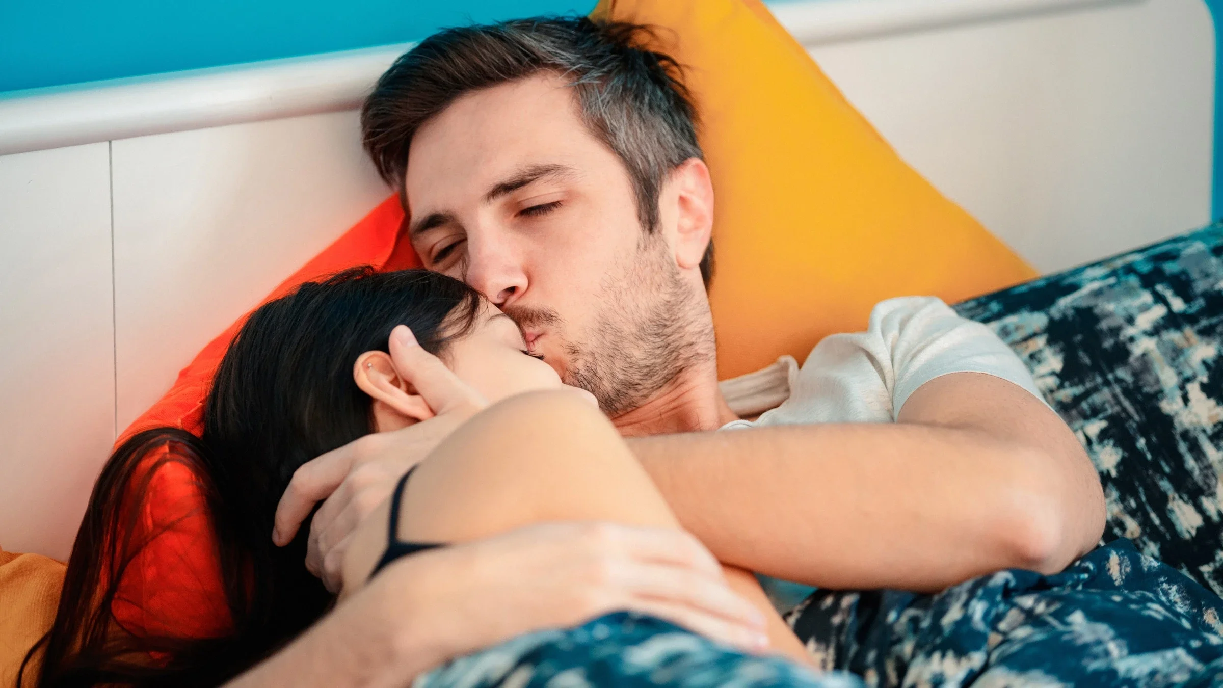 A man kissing his girlfriend's forehead to comfort her in bed.