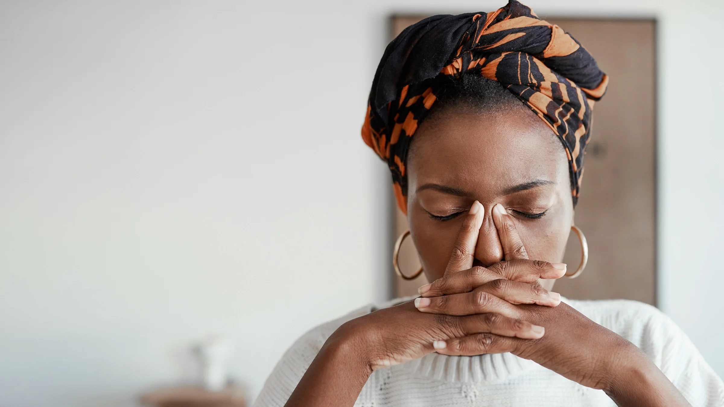 Young Black woman with a headwrap holding her hand together at her face looking in pain.