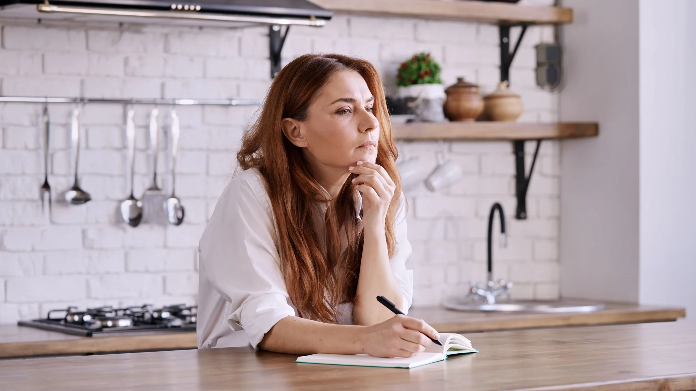 A woman writes in her notebook in the kitchen. 