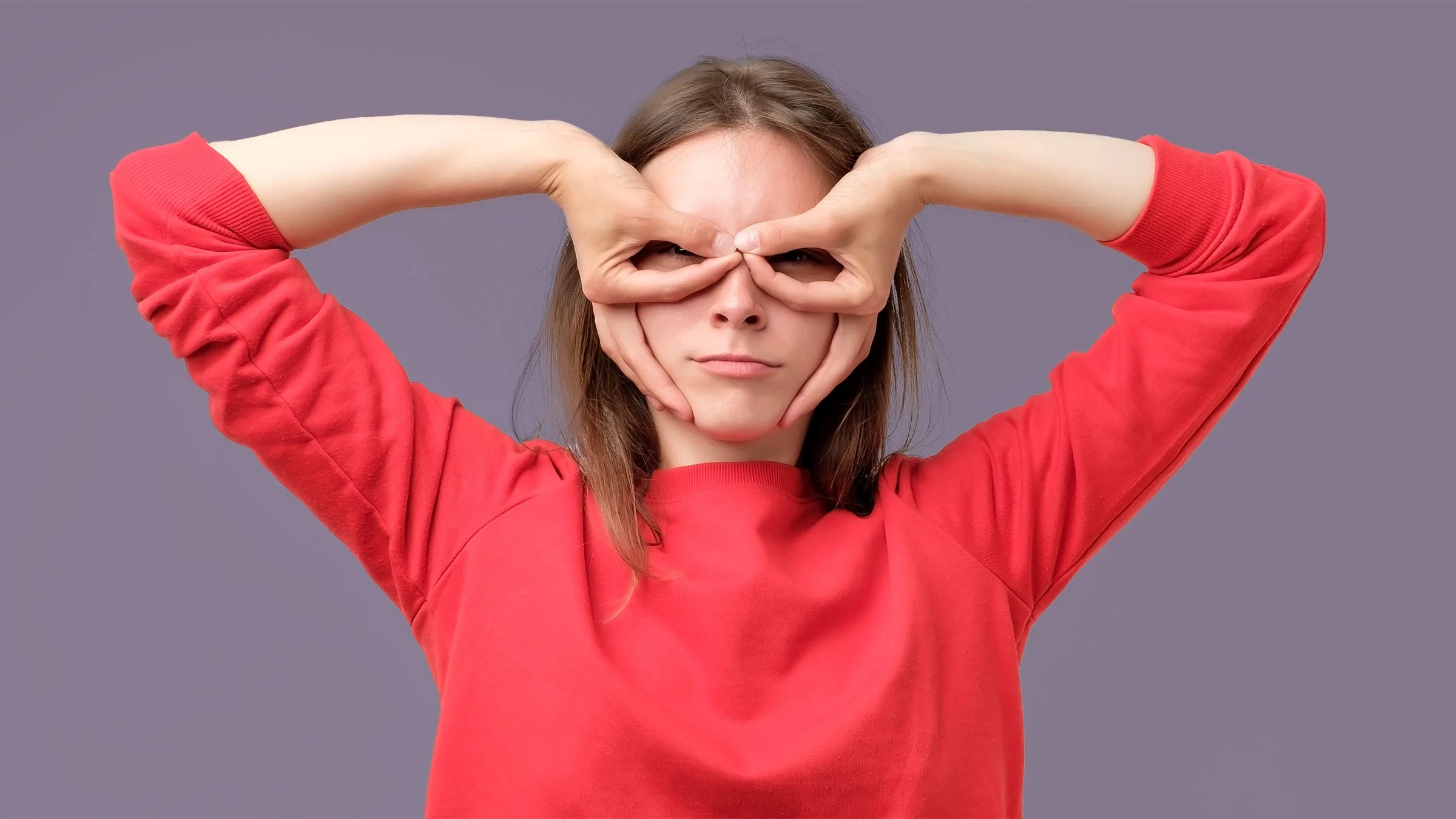 A woman in a red sweater holds her fingers near her eyes like glasses.