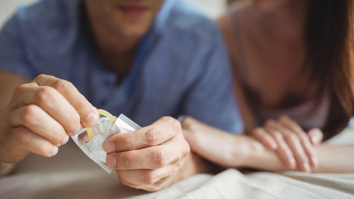 A cropped shot of a blurry couple opening a condom.