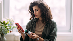 Woman holding a bottle of vitamins in one hand while looking at a smartphone.
FreshSplash/E+ via Getty Images