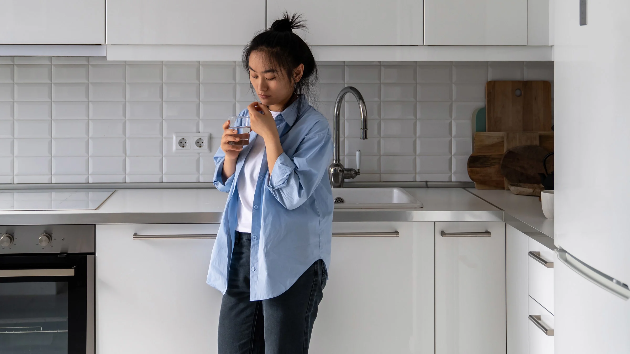 A person taking a pill in their kitchen.