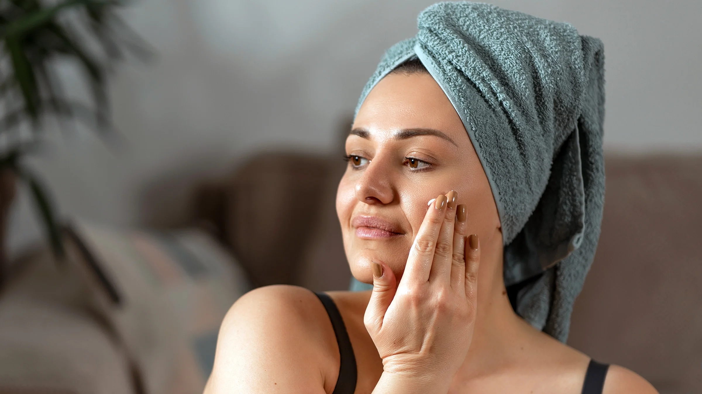Woman with a towel wrapped around her head applies face cream.