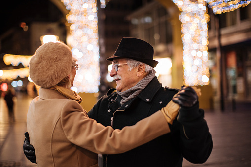 Elderly couple dancing in the street lit up with Christmas lights all around.