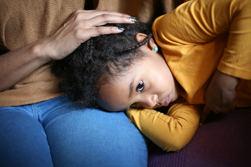 Close-up on a young girl, around four or five years old, with her head in her mother's lap.