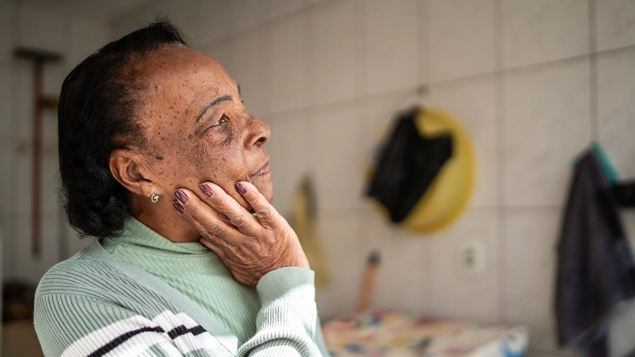 A contemplative senior woman in her home looks away.
