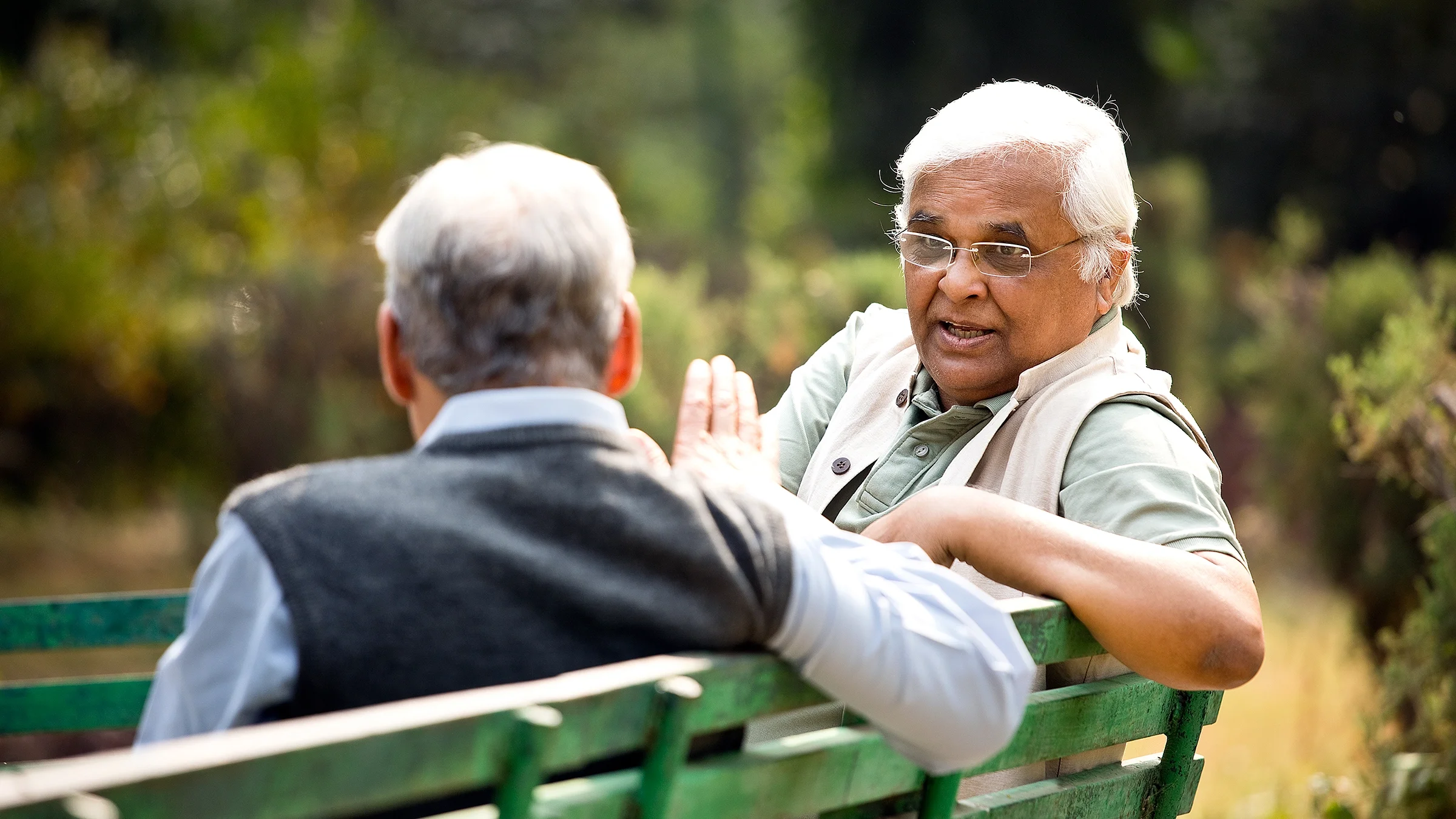 Older men talking on a green park bench.