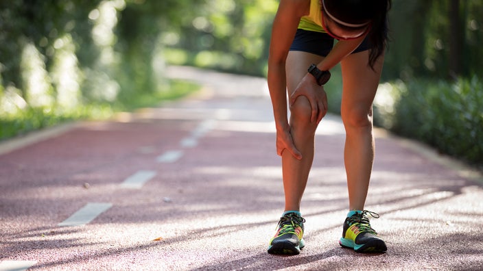 Cropped shot of a person on a trail run. They are stopping to rub their shin because they have shin splints.