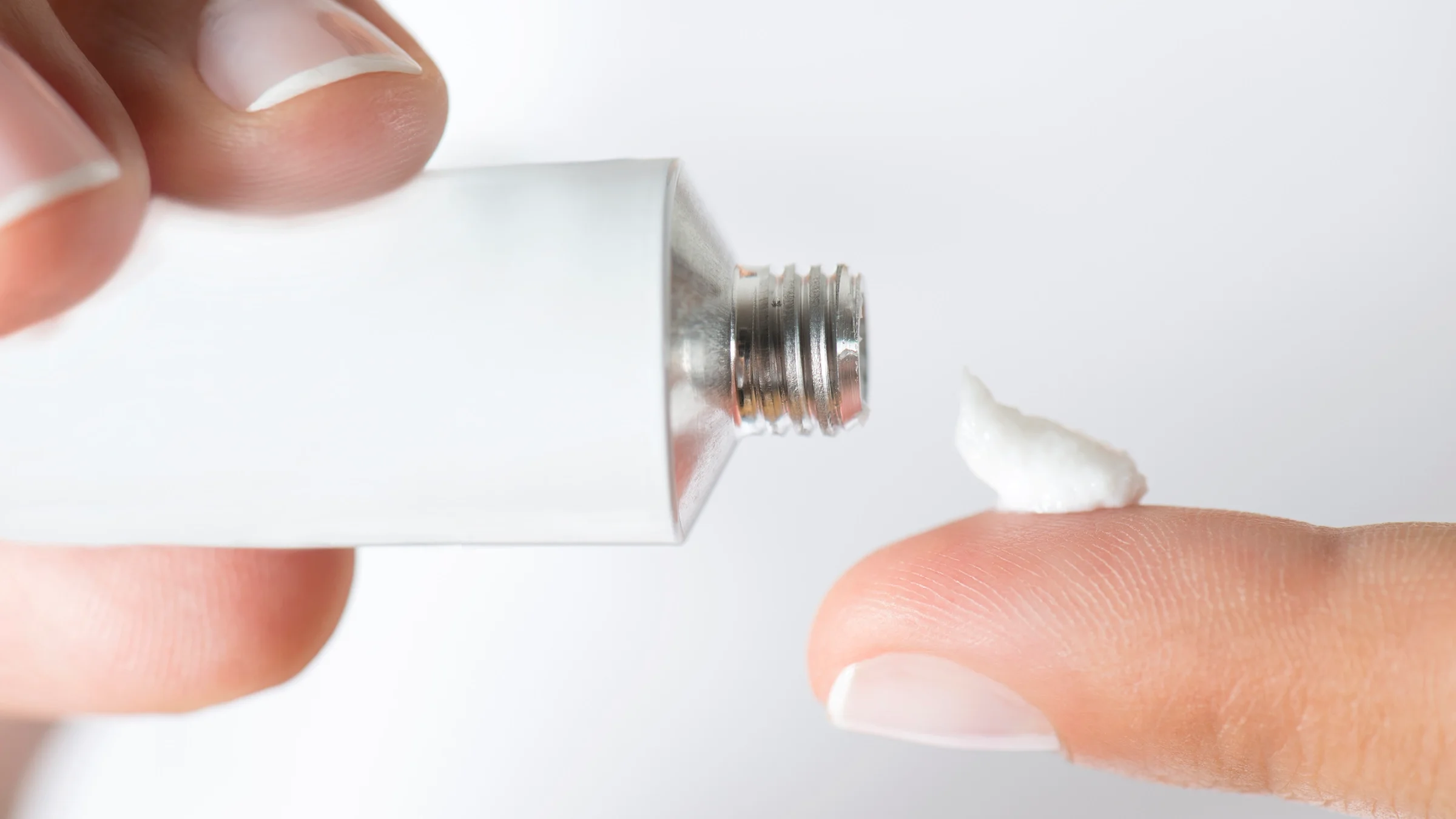 White ointment tube with white cream on finger tip on white background.