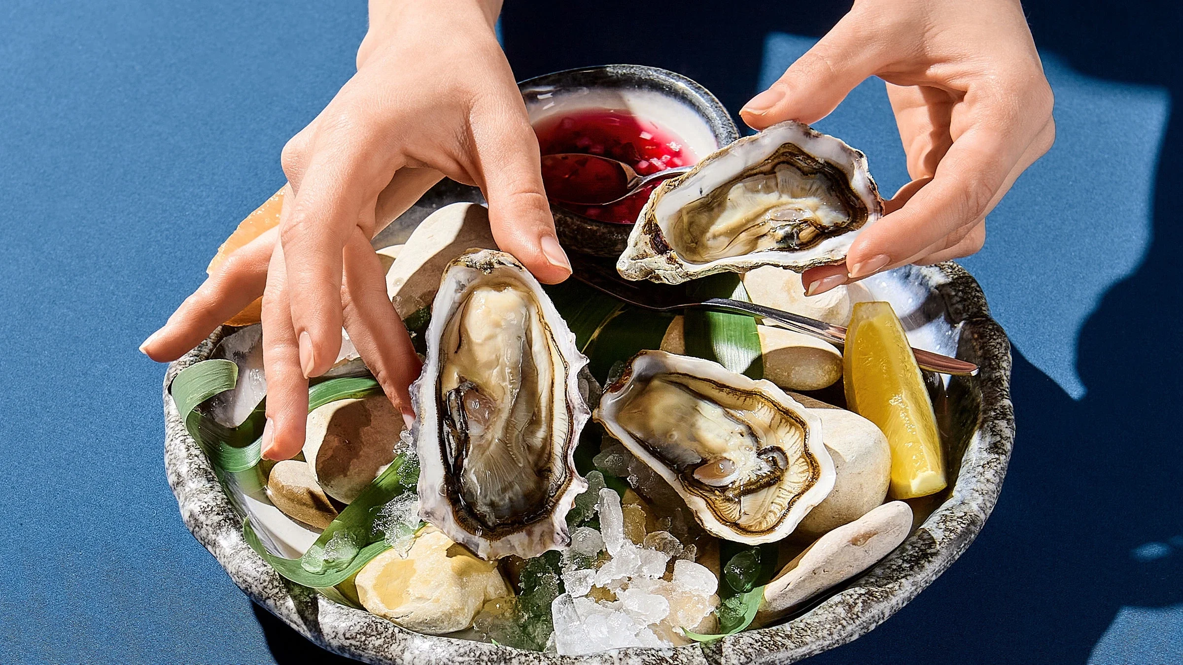 A woman picks up a fresh oyster. Oysters along with eggs, avocados, and yogurt are some of the foods that can promote hair growth. 
