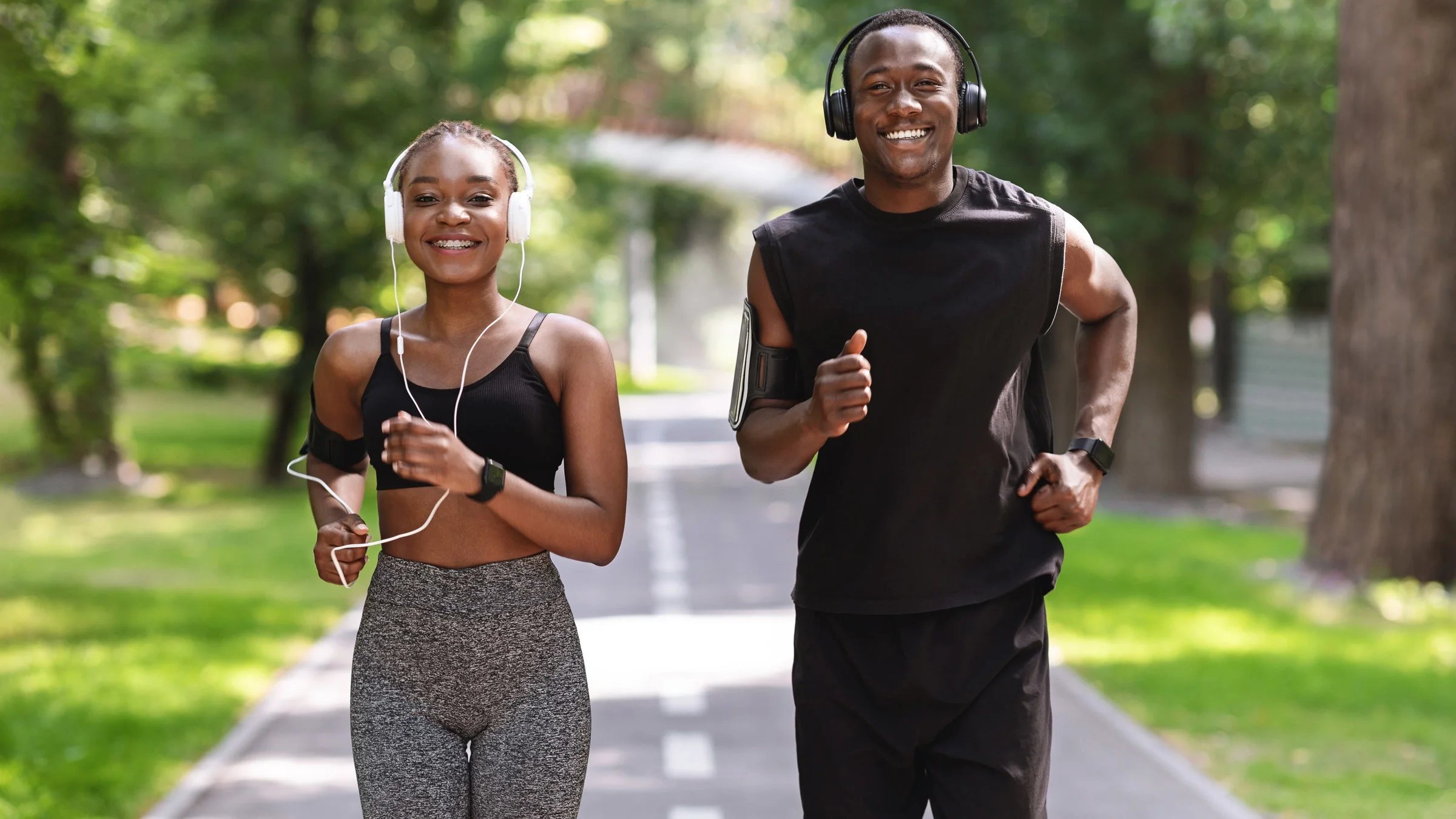 A young woman and young man running outside, wearing headphones. They are both wearing black workout clothes. 