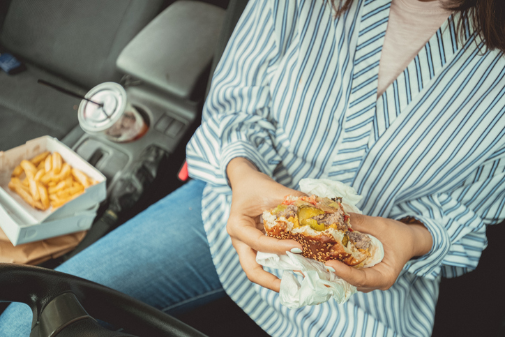 Close-up cropped shot of a woman sitting in her car eating a fast food burger meal.