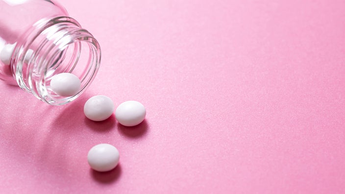White round pills on a pink background with a glass pill bottle in the corner.