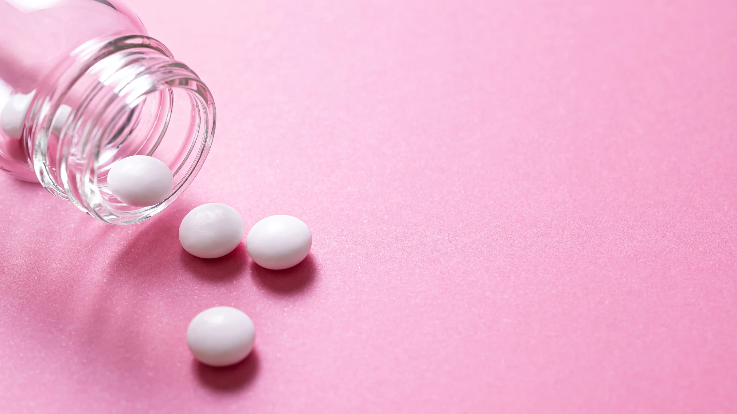 White round pills on a pink background with a glass pill bottle in the corner.